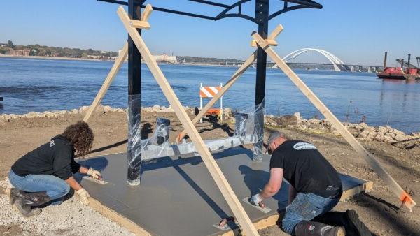 2 people smoothing out concrete pad at picnic table shelter